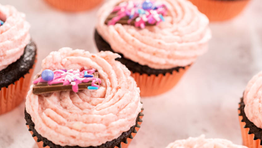 Packaging freshly baked chocolate strawberry cupcakes garnished with gourmet mini pink chocolates into a white paper cupcake box.