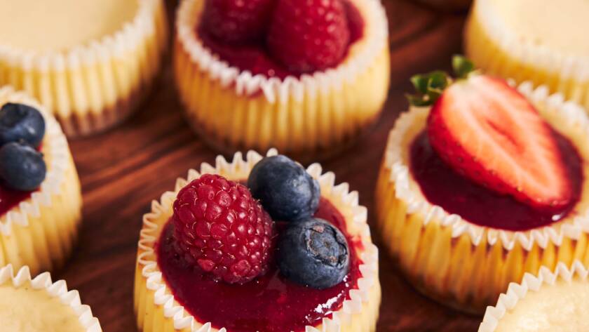 A high angle shot of cheese cupcakes with fruit jelly and fruits on a wooden plate with a white background